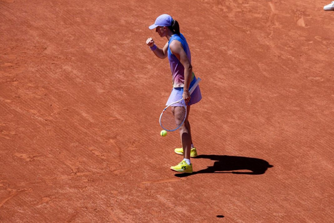 Iga Świątek z zaciśniętą pięścią na korcie ziemnym.