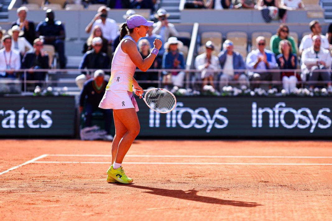 Iga Świątek z zaciśniętą pięścią na korcie ziemnym.